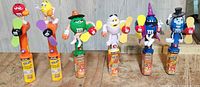 Photo of 6 M&M's candy dispensers each topped with a character in Halloween themed costumes including mummy, witch, and wizard. The dispensers have attached spinning yellow propellers. Characters are Bright Green, Yellow, Blue, Orange, Red, and Dark Blue with hats and props.