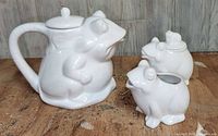 Photo of all three items: frog teapot, creamer, and sugar bowl, white ceramic on wooden surface.