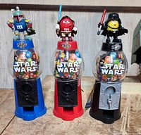 Photo of three Star Wars themed M&M dispensers featuring Boba Fett, Obi-Wan Kenobi, and Darth Vader characters. Each dispenser contains multi-colored M&Ms in a clear container with Star Wars logo.