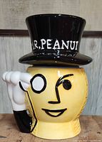 Close-up of ceramic Mr. Peanut cookie jar showing yellow peanut-shaped face with black painted features and black top hat lid with white Mr. Peanut lettering.