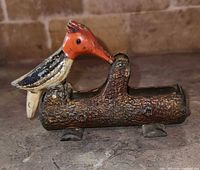 Image of a vintage metal toothpick holder shaped as a woodpecker on a tree log base with visible paint wear.