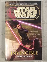 Front cover of the Star Wars Legacy of the Force Invincible paperback book showing characters with lightsabers and title details.