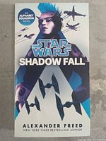 Front cover of the Star Wars Shadow Fall novel showing the character with blue hair and starships
