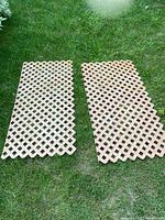 Two light brown plastic lattice garden trellis panels laid flat on grass, showing full panels with scalloped edges.