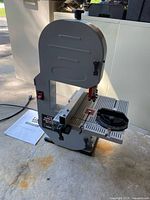 Full profile view of the band saw sitting on floor with power cord and manual visible.