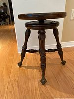 Front view of the antique wooden adjustable piano stool showing turned legs and claw and ball feet