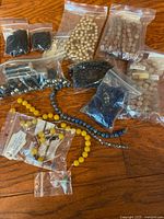 Multiple plastic bags and strands of assorted beads in various materials and colors laid out on a wooden surface