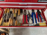 Drawer of assorted hand tools showing wood chisels and punches with wooden and plastic handles on the left, various pliers and wire cutters on the right.