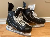 Side view of Bauer Supreme One.40 adult hockey skates showing black boot with white laces and stainless steel blade on white holder.