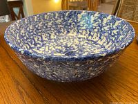 Side angle showing exterior and rim of blue and white spongeware ceramic bowl on wooden surface