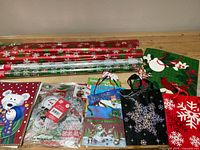 Multiple Christmas-themed gift wrap rolls, assorted gift bags, and gift tags arranged on a flat surface, showing various colors and designs
