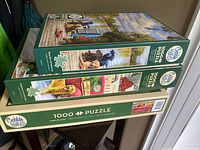Three stacked Cobble Hill puzzle boxes showing side art and puzzle piece count of 1000, themes dogs, farm, trucks