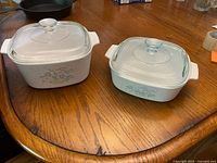 Both CorningWare Cornflower Basket casserole dishes with glass lids shown side by side on table.