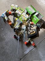 Various garden hose nozzles, connectors, stakes, and timer boxes spread on concrete floor.