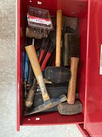 Photo of red tool chest drawer containing multiple hammers and mallets with wooden handles and rubber heads, plus wire brushes.