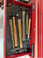 Full overview of all 8 items in the tool drawer, showing claw hammers, ball-peen hammers, handles, and specialty pieces including a small tack hammer and partial brass hammer head/handle.