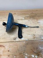 Full side view of the manual drain snake showing ergonomic handle, circular housing, and metal snake with spiral tip.