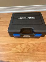Closed black hard plastic carrying case with Mastercraft branding and blue latches, holding the nailer and accessories inside.