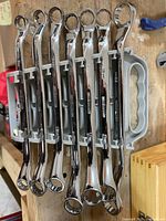 Nine Mastercraft metric combination wrenches arranged horizontally in gray plastic holder with handle, showing both open and box ends.