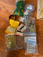 Mixed assortment of craft supplies arranged on wooden surface. Includes bags of chain links, cords, and jewelry findings in plastic bags, some cords coiled, plastic bags with small metal accessories.