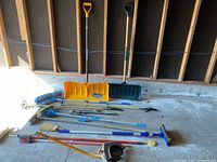 Wide shot of all tools laid out showing various yard and cleaning tools including shovels, brooms, and brushes.