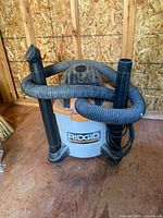 Front angle showing RIDGID wet/dry vacuum with wrapped hose and extension wands attached to vacuum base.