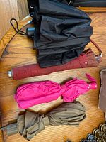 Four folded umbrellas placed on a wooden surface showing black, red, pink, and brown colors with different handle types and some wear visible.
