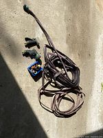Entire lot showing two coiled soaker hoses, two spray nozzles, and blue container with hose connectors and fittings in sunlight on concrete floor.