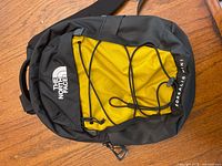 Front view of The North Face Borealis Mini backpack showing black and yellow nylon fabric, front elastic bungee cord, white logo, and zipper details.