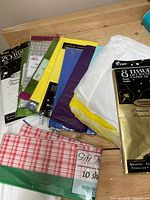 Photo showing multiple tissue paper packs stacked, featuring white, yellow, purple, blue, green, and pink checked tissue sheets visible.