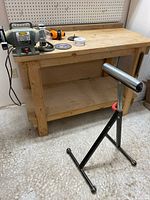 Full view of wooden workbench with the Trademaster bench grinder on top and part of the Wolfcraft roller stand in front.