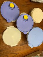 Top view showing blue and cream lids with yellow vent buttons on some containers, arranged on wooden surface.