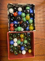Top-down photo showing two boxes filled with marbles of various colors and patterns, one with solid and speckled colors, the other with clear glass and swirled colors.