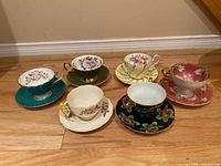 Six vintage teacup and saucer sets arranged on floor showing assorted patterns and colors