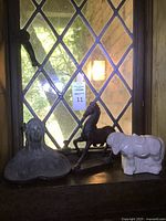 Overview photo of all three items together on a windowsill: bust of woman on the left, dark horse statue in middle, white pony planter on right.