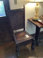 Front full view of antique wooden chair with carved human figure finials and detailed back panel.