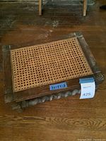 Photo showing footstool from a side angle highlighting the woven cane top and wooden frame with carved twisted wood details on the legs and base.