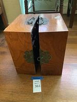 Front view of the closed apothecary chest showing wood grain and ornate metal door hardware with handles.