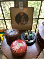Framed artwork behind lacquer boxes and figurines on a table near window