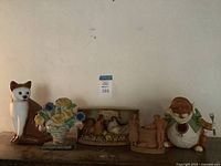 Five assorted ceramic and cast iron figurines shown on wooden surface with white wall background.