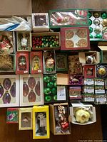 Full lot overview showing several boxed and loose Christmas ornaments of various shapes, colors and brands arranged on a table.