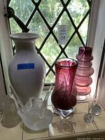 Photo of assorted decorative vases and glassware on a windowsill showing height variety and colors including white ceramic and purple glass vases.