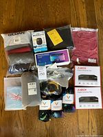 Overview of assorted new and sealed items including clothing, electronics, and socks on a wooden floor.