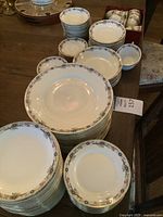 Wide shot showing stacks of dinner plates, soup bowls, dessert plates, teacups, and saucers arranged on a table