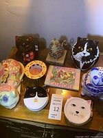 Overview photo showing most of the cat-themed items arranged on a wooden table, including maneki-neko cat, colorful mosaic cat, blue and white jar, and cat face dishes.