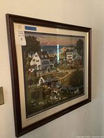 Framed wall artwork showing colorful village scene with houses, trees, people, and animals.