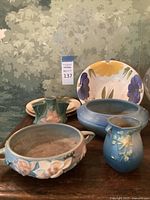 Full view of lot items including the blue oval bowl, round pottery bowl, blue vase, dual-spout green vase, and large hand-painted floral plate.