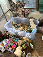 Wide shot showing large plastic bin filled with assorted small decor pieces including figurines, Easter eggs, and containers, surrounded by larger bunny cutouts and a floral tray.