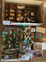 Overhead view of two compartmented boxes containing assorted hand-painted glass ornaments (insect, animal, novelty).