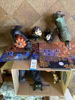 Overview photo showing several cat figurines and two Halloween-themed paintings arranged on floor.